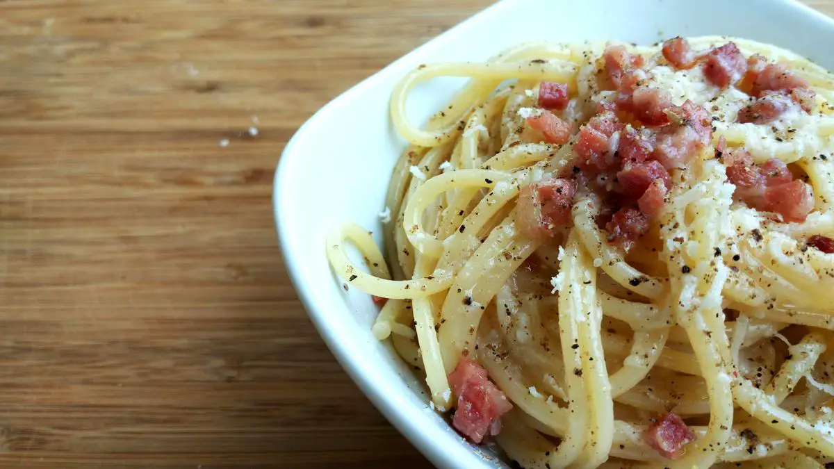 Un plato de pasta carbonara con trozos de guanciale crujiente, servido con queso pecorino rallado y pimienta negra molida.